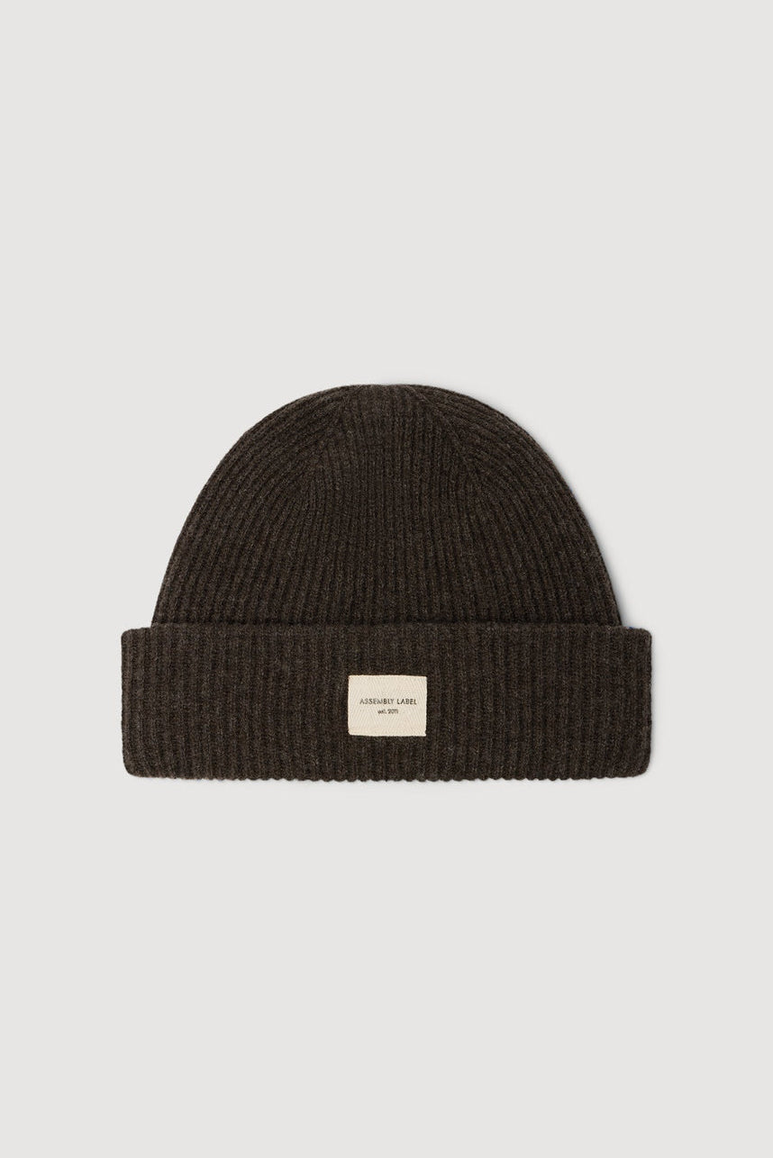 Dark brown knit beanie with a small label on a light gray background