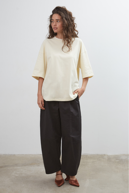 Woman wearing a pale yellow top and black pants against a white background