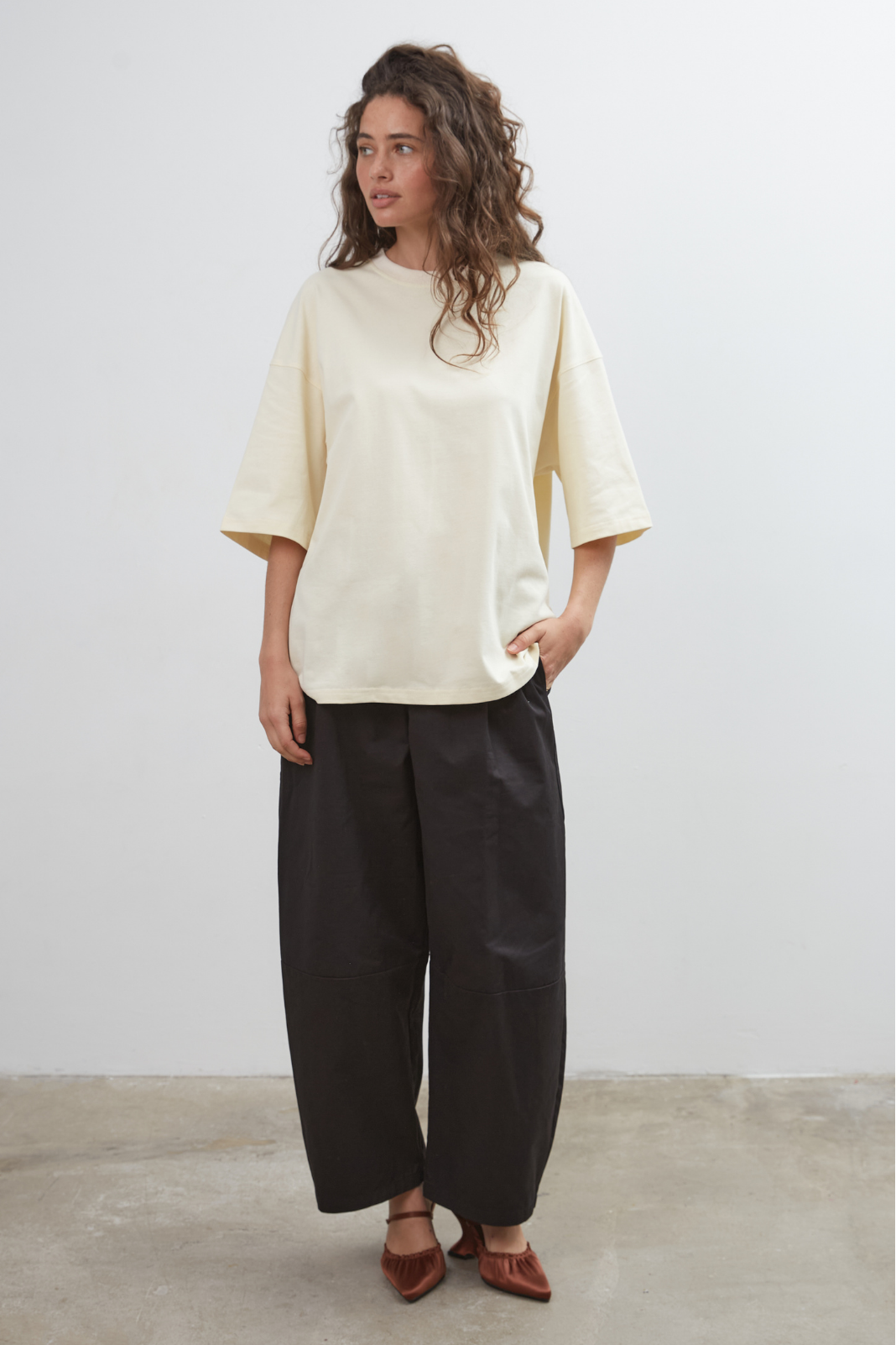 Woman wearing a pale yellow top and black pants against a white background