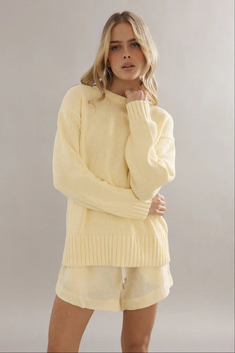 Woman wearing a light yellow sweater and shorts against a plain background