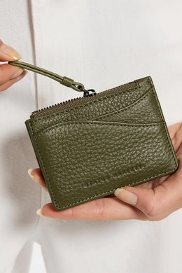 Green textured wallet held by a person against a white background