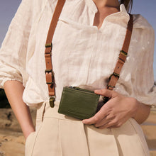 Person holding a green wallet with a brown strap against a blurred natural background